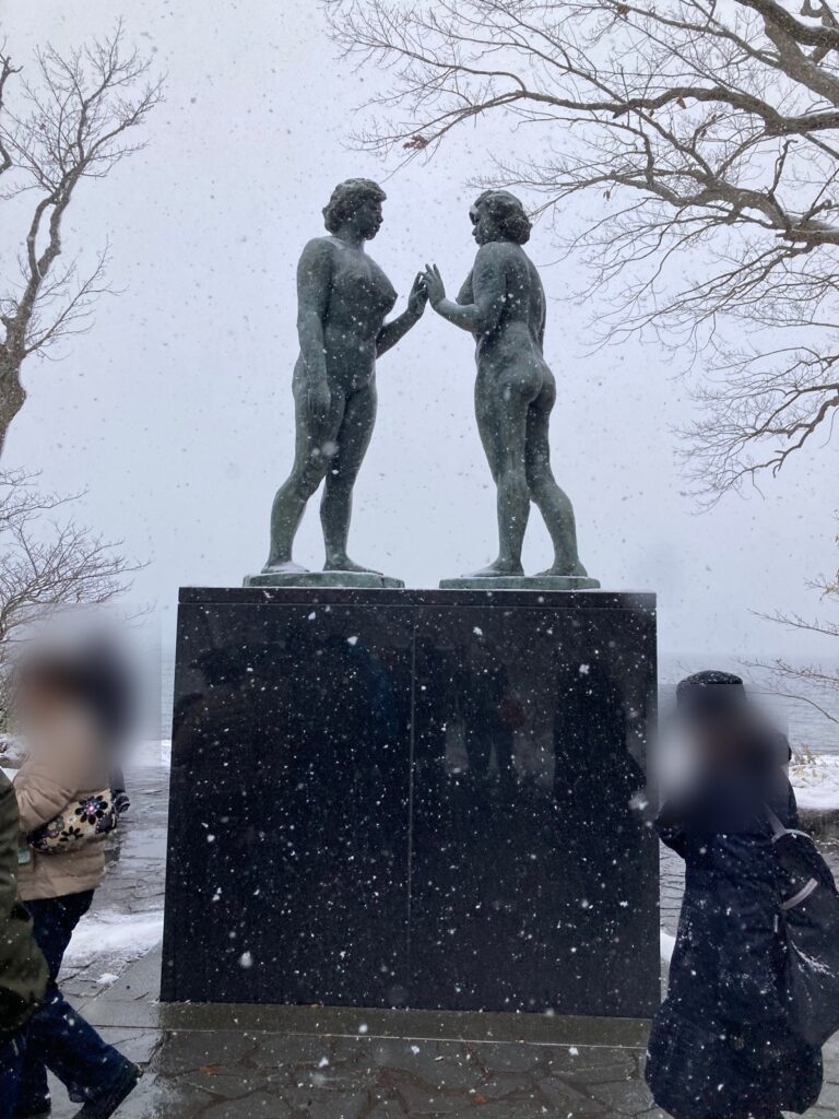 雪が降る十和田湖畔に立つ乙女の像